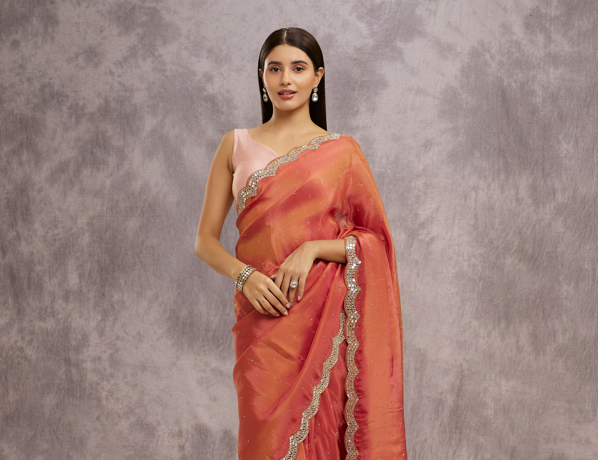 Woman in a rust-orange silk saree with subtle embellishment and a plain pink sleeveless blouse.